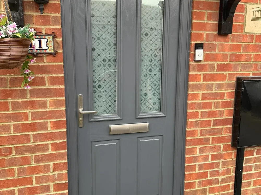 Grey composite front door with decorative glass and a new handle on a brick house
