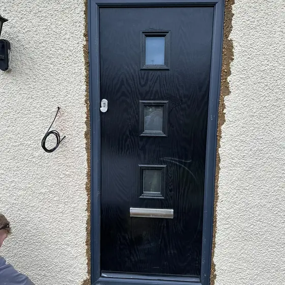 Anthracite composite door with small glazed squares fitted to a rendered house