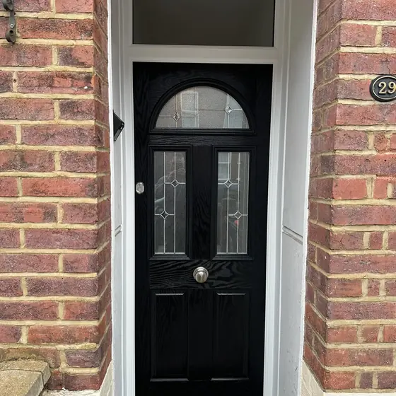 Black composite door with arched decorative glass and top light in a brick porch