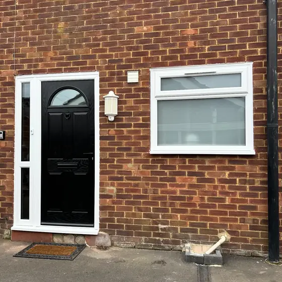 Black composite front door with arched glass in a white frame with side panel