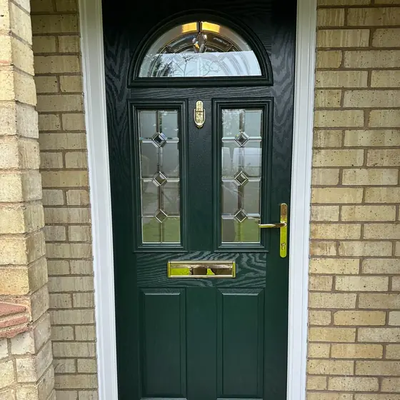 Dark green composite front door with arched decorative glazing and gold furniture