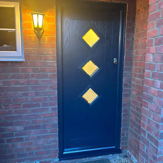 Navy composite front door with three diamond glass panels under a porch light