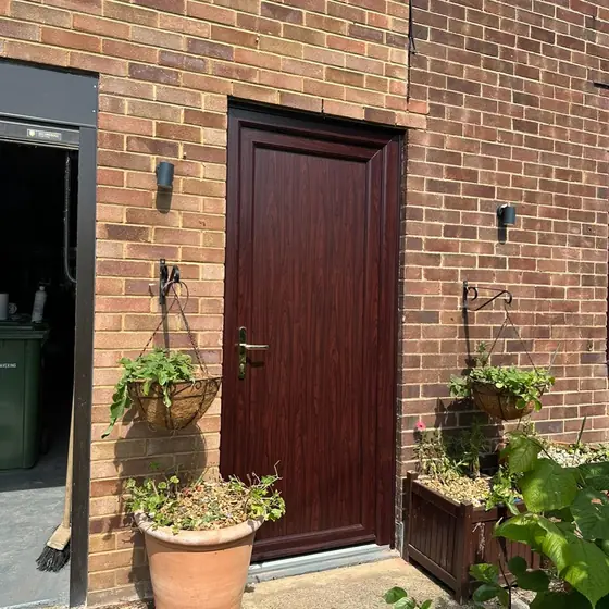 Rosewood-finish front door on a brick house with planters